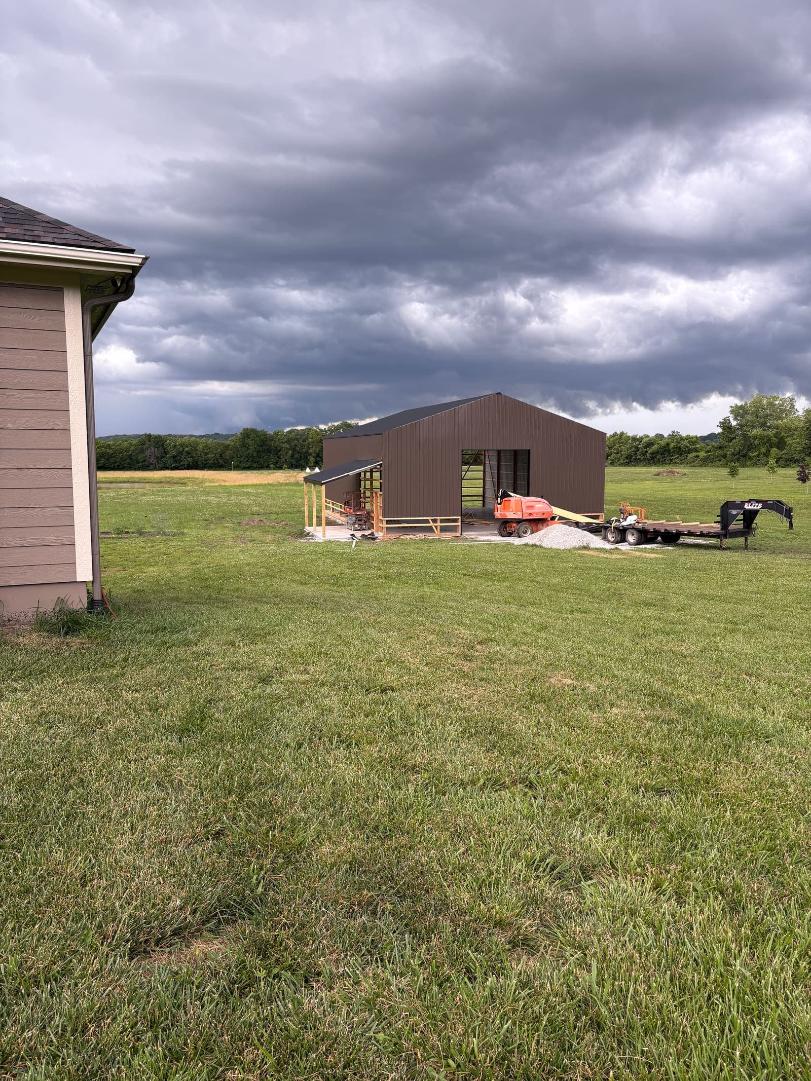 Equipment staged at a rural pole barn site under storm clouds