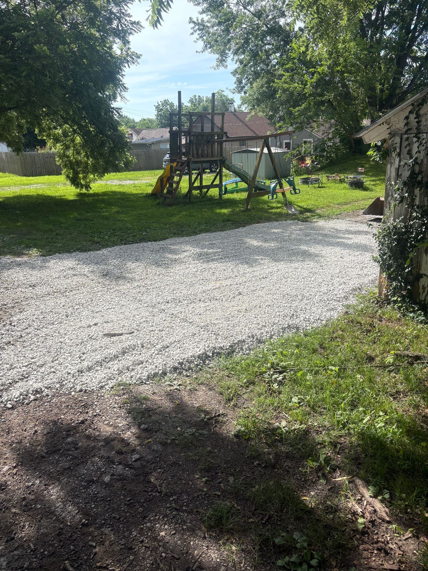 New gravel parking area beside a backyard playset